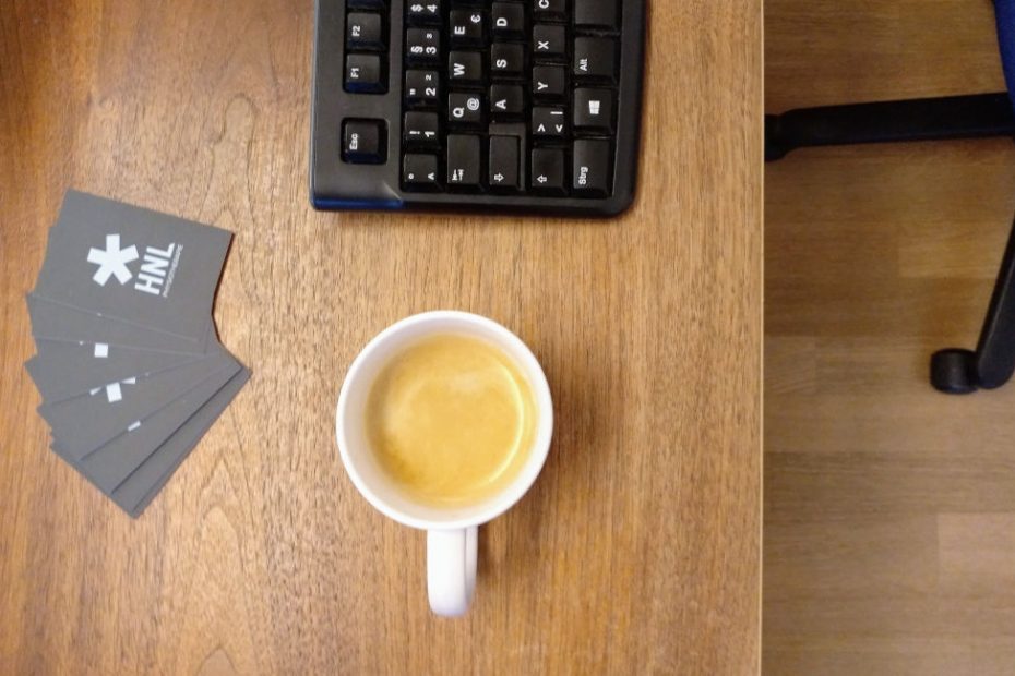 Schreibtisch mit Tastatur, Kaffeebecher und Visitenkarten eines Physiotherapeuten